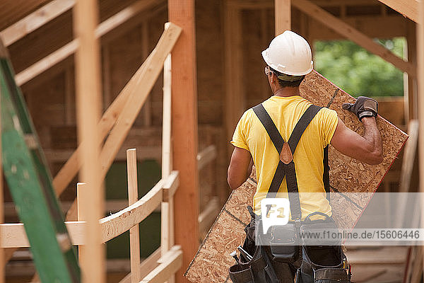 Hispanic carpenter holding a roof panel at a house under construction
