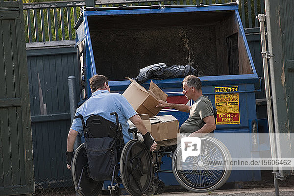 Männer in Rollstühlen mit Rückenmarksverletzungen  die Müll in einen Müllcontainer werfen