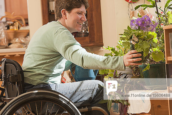 Frau mit Multipler Sklerose im Rollstuhl gießt Zimmerpflanzen