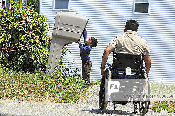 Hispanischer Mann mit Rückenmarksverletzung im Rollstuhl mit seinem Sohn schaut in einen Briefkasten