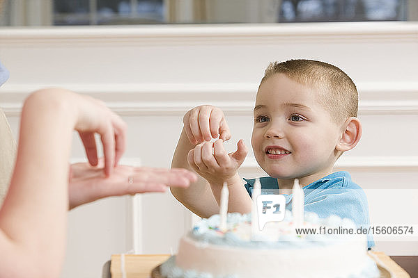 Boy signing the word 'Cake' in American sign language sitting in front of a birthday cake