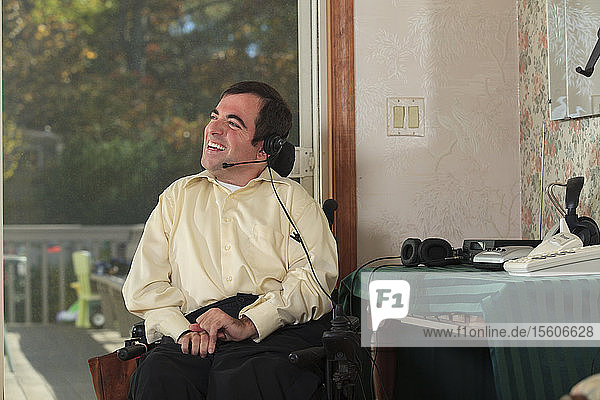 Mann mit Cerebralparese im motorisierten Rollstuhl benutzt sein Telefon-Headset