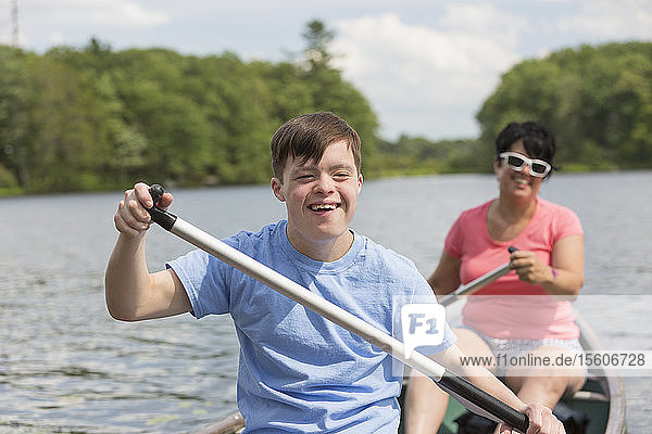 Junger Mann mit Down-Syndrom rudert mit seinem Freund in einem Kanu auf einem See