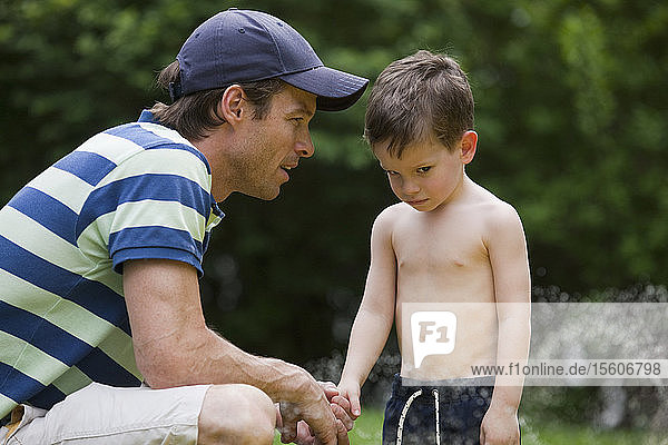 Man talking to unhappy son after running through the water hose