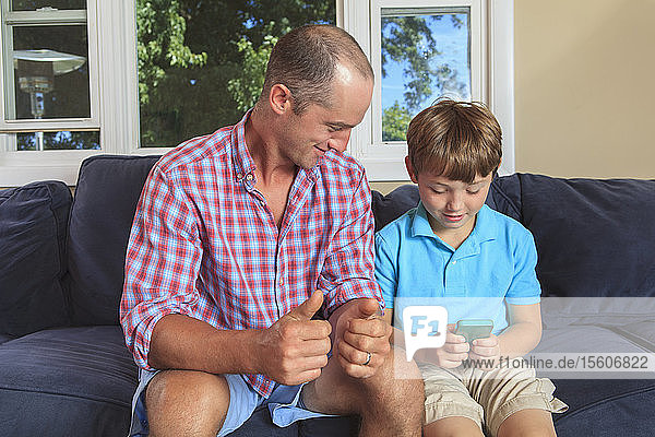 Vater und Sohn mit Hörbehinderung geben auf der Couch Text in amerikanischer Gebärdensprache auf dem Mobiltelefon aus