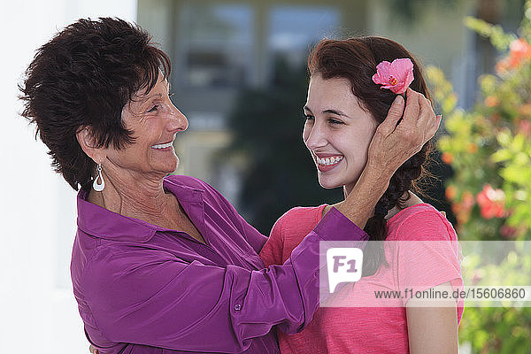 Ältere Frau  die lächelnd eine Blume im Haar ihrer Enkelin zurechtrückt