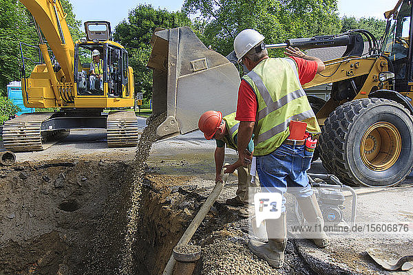Bauarbeiter füllen ein Loch mit Kies vom Frontlader