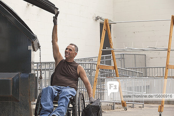 Laderampenarbeiter mit Rückenmarksverletzung im Rollstuhl  der eine Tasche in den Müllcontainer wirft