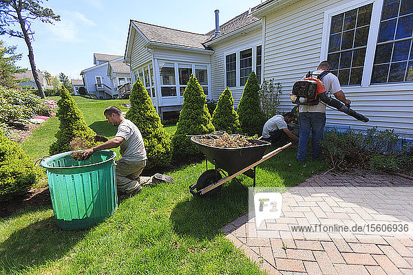 Landschaftsgärtner bei der Unkrautbekämpfung in einem Hausgarten und beim Einsatz eines Gebläses zur Reinigung