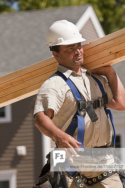 Carpenter carrying wall studs at a construction site