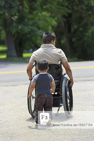 Hispanoamerikanischer Mann mit Rückenmarksverletzung im Rollstuhl mit seinem Sohn
