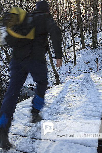Hiker crossing snow covered bridge at Hemlock Gorge Newton Massachusetts USA