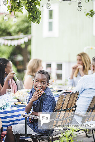 Lächelnder Junge isst Wassermelone  während er mit der Familie in der Gartenparty sitzt