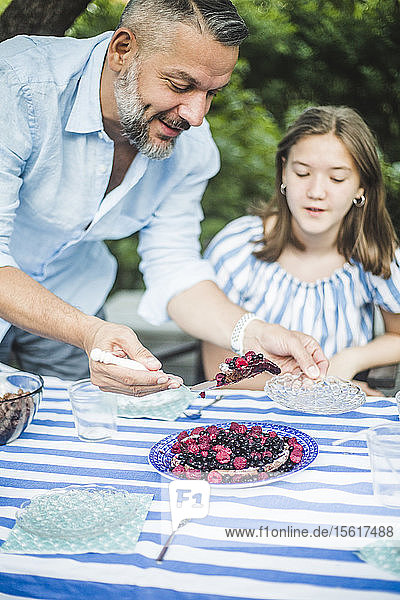 Man serving berry tart to daughter at table in backyard