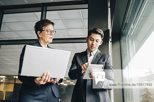 Male executive showing digital tablet to senior professional while standing in office