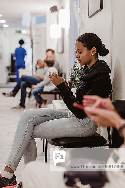 Mädchen benutzt Mobiltelefon während des Wartens im Krankenhauskorridor