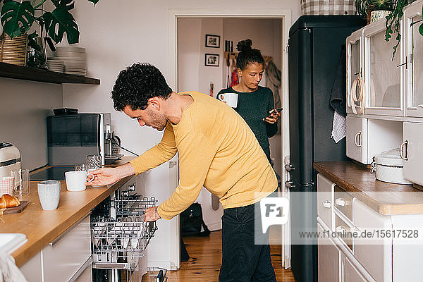 Mittelgroßer Erwachsener  der zu Hause eine Tasse aus der Schublade unter der Küchentheke entnimmt