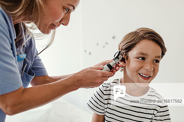 Arzt untersucht Ohr des Jungen mit Otoskop im medizinischen Untersuchungsraum
