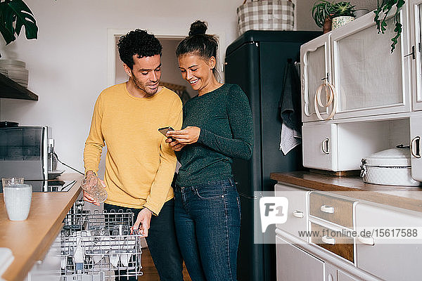 Frau lächelt  während sie ihrem Freund ein Smartphone zeigt  während sie in der Küche steht
