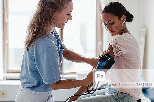 Reife Krankenschwester prüft den Blutdruck des Patienten im Untersuchungsraum der Klinik