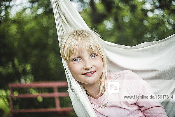 Porträt eines lächelnden Mädchens  das in einer weißen Schaukel im Garten sitzt