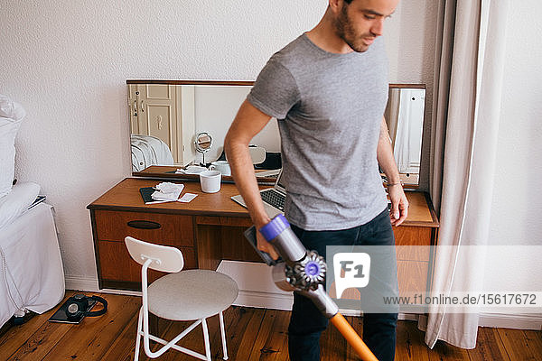 Mid adult man cleaning bedroom with vacuum cleaner