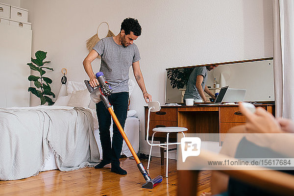 Mann reinigt Schlafzimmer in voller Länge mit Staubsauger
