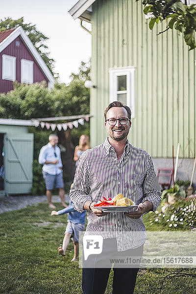 Porträt eines lächelnden  reifen Mannes  der im Hinterhof steht und einen Speiseteller hält