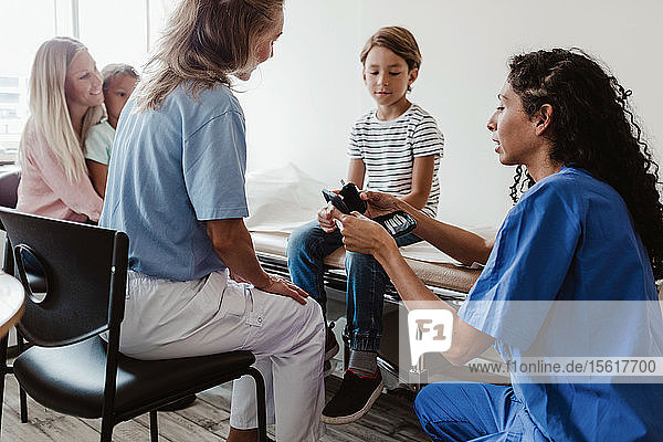 Krankenschwester und Ärztin zeigen dem Jungen ein Glaukometer  während die Familie in der Klinik sitzt