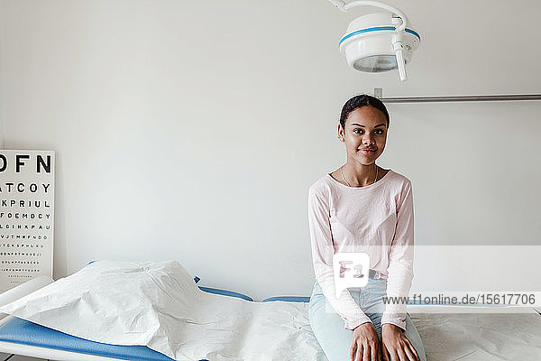 Porträt eines lächelnden Mädchens  das auf dem Untersuchungstisch im Krankenhaus sitzt