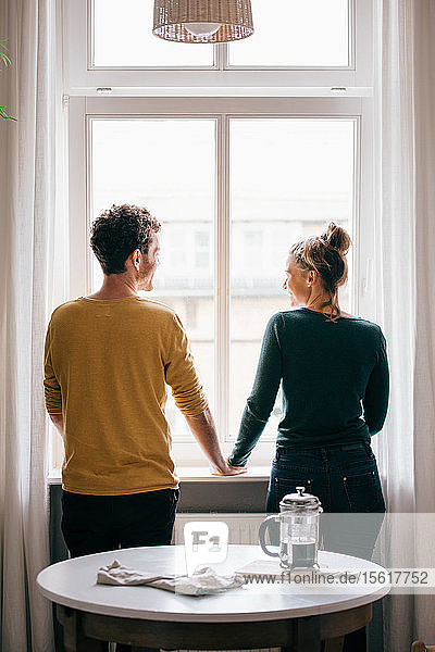 Rückansicht eines am Fenster stehenden romantischen Paares im Wohnzimmer