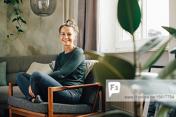 Porträt einer lächelnden Frau  die zu Hause auf einem Sessel sitzt