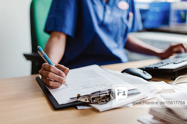Mittelteil einer Krankenschwester  die einen medizinischen Bericht schreibt  während sie in der Klinik am Schreibtisch sitzt