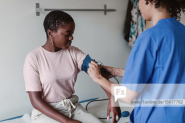 Nurse checking blood pressure of female patient in clinic