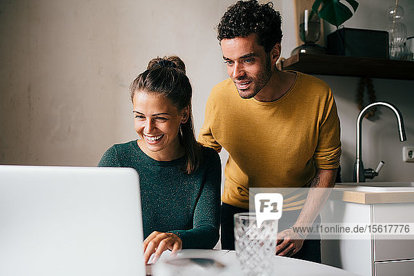 Boyfriend and girlfriend smiling while looking at laptop on table