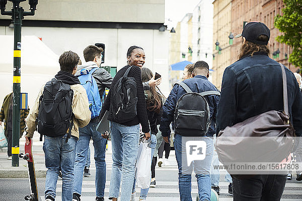 Rear view of teenage friends crossing street in city
