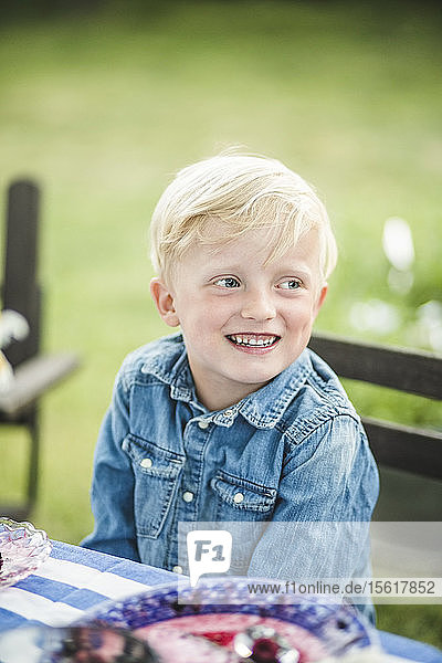 Lächelnder Junge schaut weg  während er im Garten am Tisch sitzt