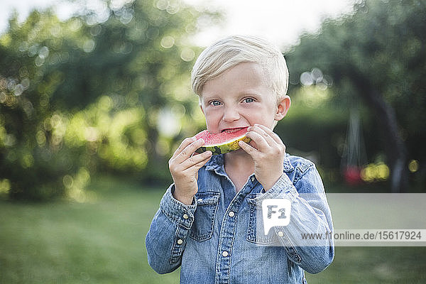 Porträt eines Jungen  der im Hinterhof frische Wassermelone isst