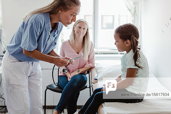 Krankenschwester im Gespräch mit einem Mädchen  das im Krankenhaus auf dem Untersuchungstisch sitzt