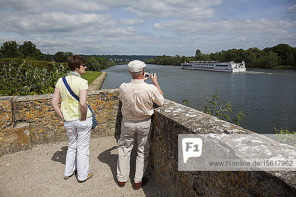 Ein Paar beobachtet die vorbeifahrenden Ausflugsboote auf der Seine von La Roche-Guyon  Frankreich.