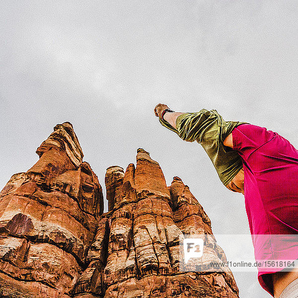 Niedriger Blickwinkel auf eine Frau  die ihre Hände über dem Kopf hat und ihr Hemd zwischen ungewöhnlichen Sandsteinformationen im Canyonlands National Park auszieht.