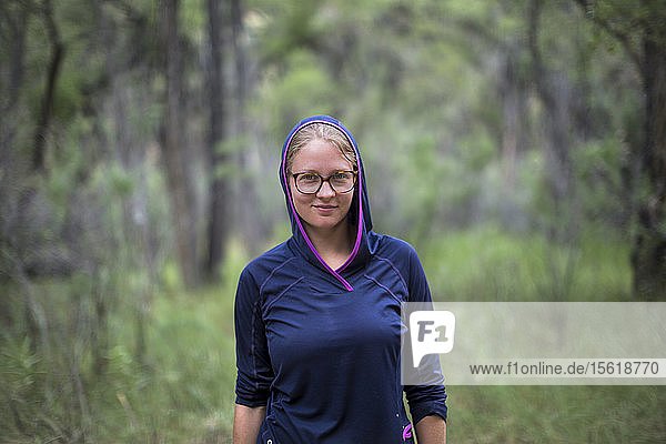 Front view waist up portrait of female raft guide in blue hooded sweatshirt and eyeglasses in forest