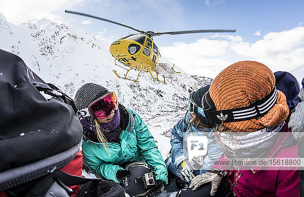 Die Profi-Snowboarder Helen Schettini  Jamie Anderson und Robin Van Gyn gehen in die Hocke  als ein Hubschrauber an einem sonnigen Tag in Haines  Alaska  neben ihnen zur Landung ansetzt.