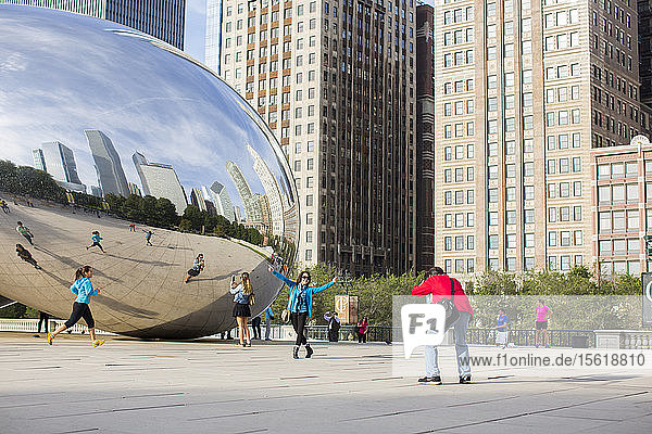 Eine erwachsene Frau läuft an der Cloud Gate-Skulptur im Millenium Park vorbei  während Touristen sich vor der Skulptur fotografieren. Chicago  Illinois.