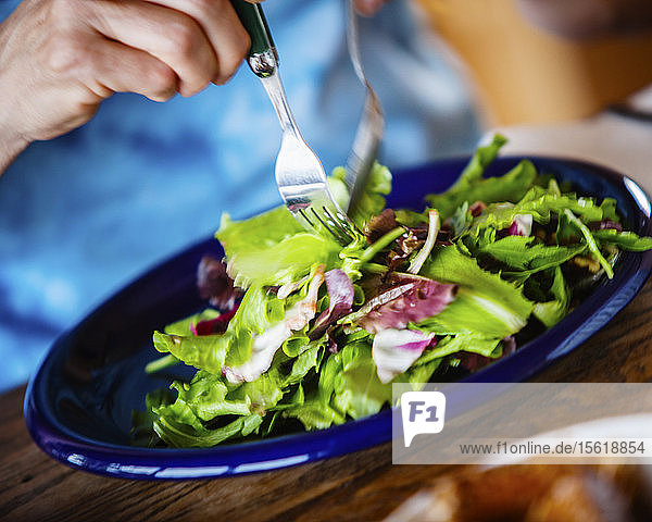 A hand  a fork and spoon  and a fresh green salad.