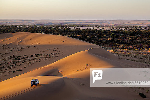 Ein Geländewagen fährt entlang einer Sanddüne im Licht der untergehenden Sonne