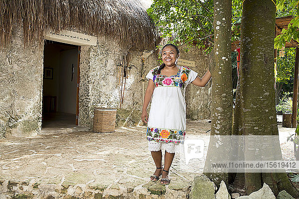 Junge lächelnde Frau in traditioneller Kleidung an einem Baum in der Nähe der Stadt Coba in Quintana Roo  Mexiko