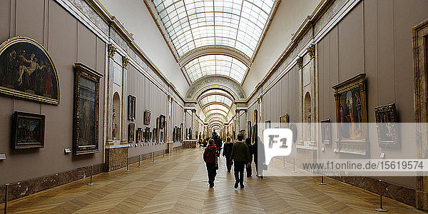 Rückansicht von Menschen  die einen mit wertvollen Kunstwerken gesäumten Innengang im Musée du Louvre entlanggehen. Paris  Frankreich.