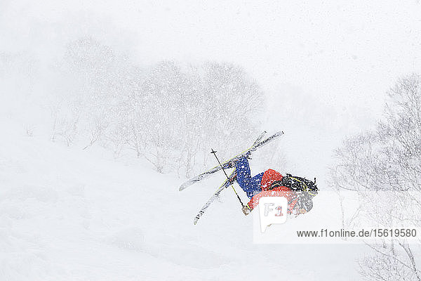 Ein männlicher Backcountry-Skifahrer fliegt kopfüber in die Luft  auf halbem Weg den Vulkan Annupuri im Skigebiet Niseko United hinunter. Er hat versucht  einen Rückwärtssalto zu machen  aber er hatte ein bisschen zu viel Geschwindigkeit. Der Schnee auf der japanischen Insel Hokkaido ist so tief und flauschig  dass er ein Paradies für Tiefschneefahrer ist und große Sprünge ermöglicht  da die Landung immer weich ist. Niseko United besteht aus vier Skigebieten auf einem Berg  dem Annupuri (1.308 m). Der 100 km südlich von Sapporo gelegene Niseko Annupuri ist Teil des Quasi-Nationalparks Niseko-Shakotan-Otaru Kaigan und ist der östlichste Park der Niseko-Vulkangruppe. Hokkaido  die nördliche Insel Japans  liegt geografisch ideal in der Bahn der beständigen Wettersysteme  die die kalte Luft aus Sibirien über das Japanische Meer bringen. Dies führt dazu  dass viele der Skigebiete mit Pulverschnee überhäuft werden  der für seine unglaubliche Trockenheit bekannt ist. In einigen der Skigebiete Hokkaidos fallen durchschnittlich 14-18 Meter Schnee pro Jahr. Niseko ist die Pulverschneehauptstadt der Welt und als solche das beliebteste internationale Skigebiet in Japan. Es bietet ein unvergessliches Erlebnis für Skifahrer und Snowboarder aller Niveaus.