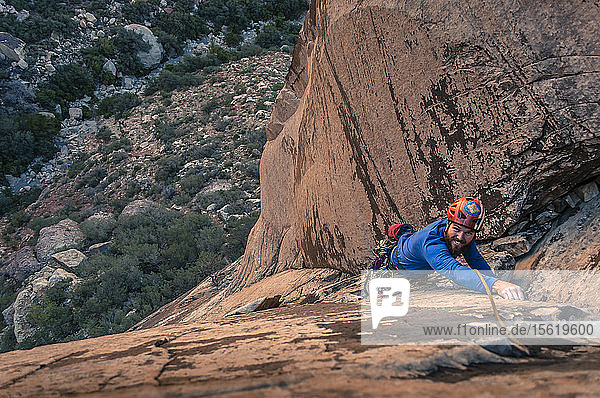 View from above of single male adventurous rock climber climbing up sandstone cliff Red Rock National Park Nevada USA